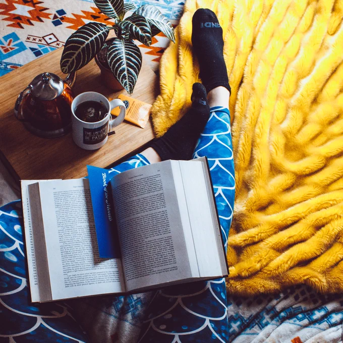 A person with a book on their knee. A coffee cup and plant.