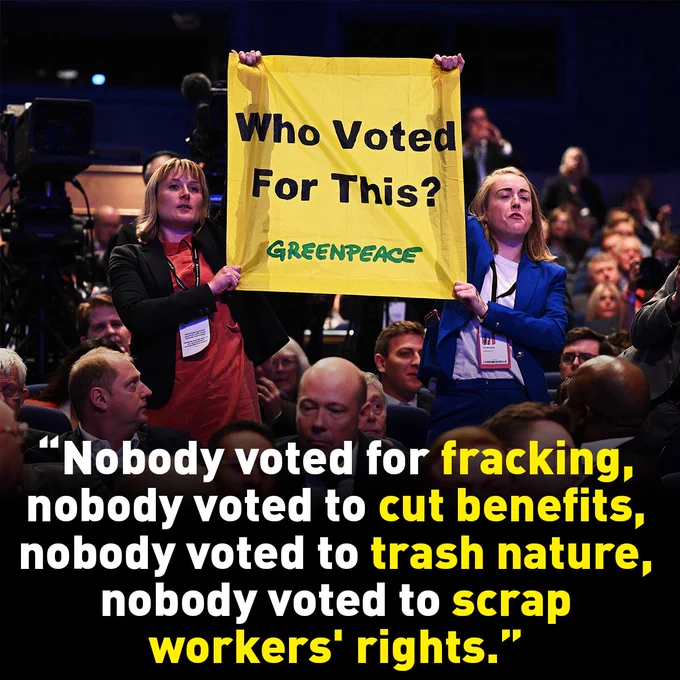 Two protesters at #CPC22 holding up a banner that says #WhoVotedForThis?