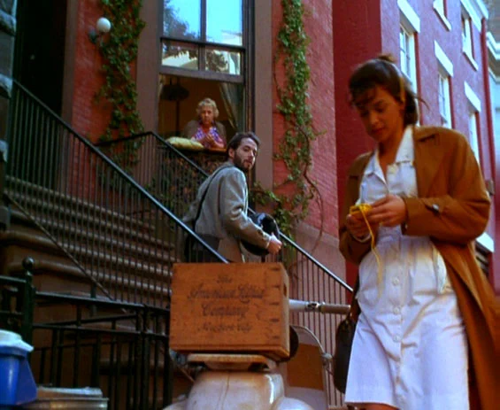 From the movie The Night We Never Met, a man is on the stairs outside of an apartment and is looking back at the woman who just passed him. An older woman is watching the exchange from her apartment window. 