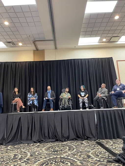 7 panelists waiting to start speaking on stage at the conference