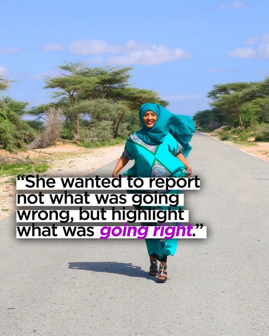 Hodan Nalayeh walking toward the camera down a tree-lined road in Somalia, smiling. Her hijab and clothes are billowing in the wind.