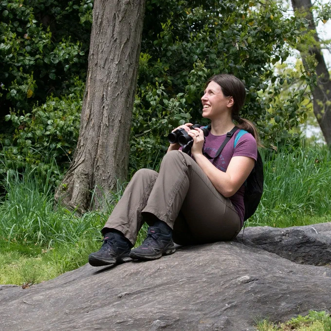a woman sits on a rocky slope holding binoculars