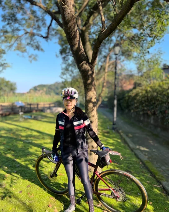 France wearing a helmet, standing outside in the grass by her bike. 