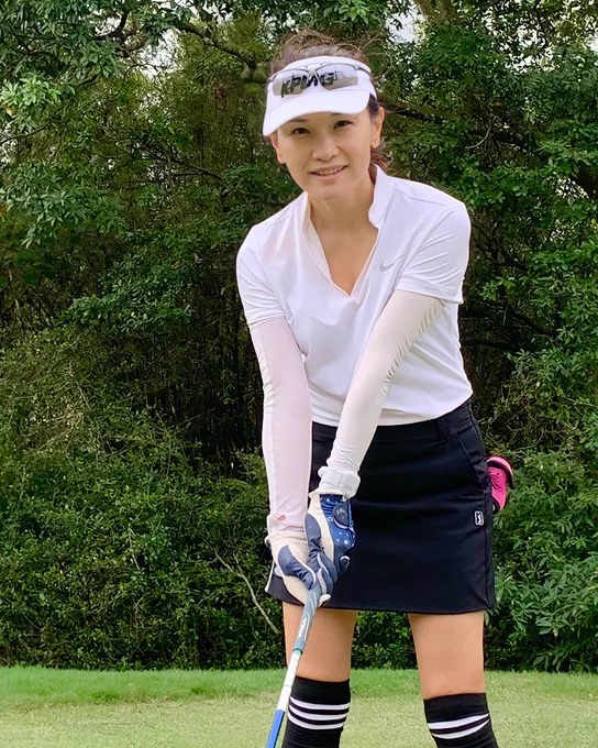 Frances wearing a white golf shirt and a black skirt standing in a ready-to-swing pose. 