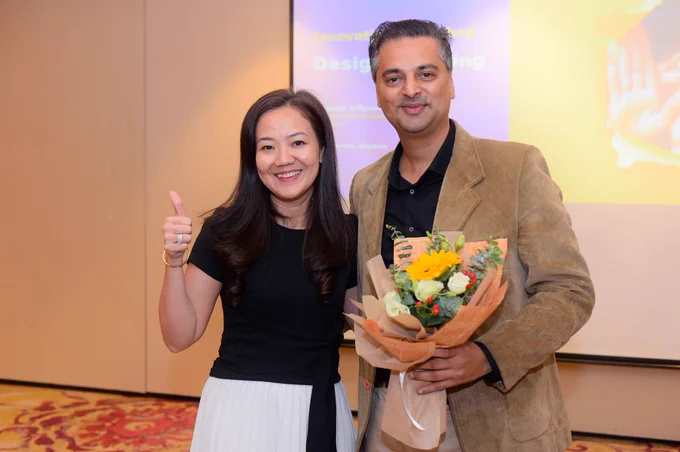 An attendee gives the thumbs up next to the presenter, who is holding flowers.
