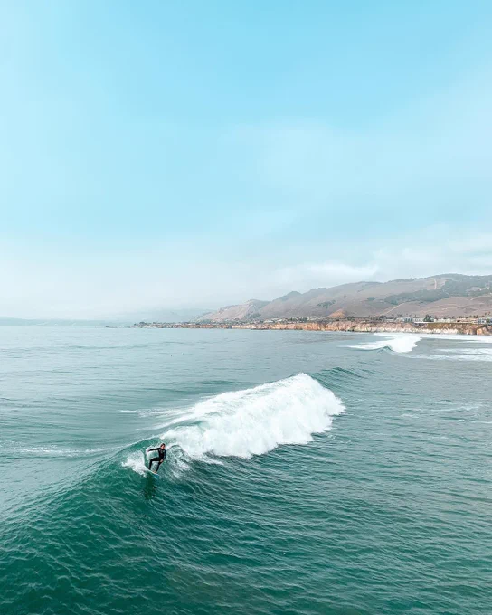 Man surfing on a sunny day with rolling hills in the background