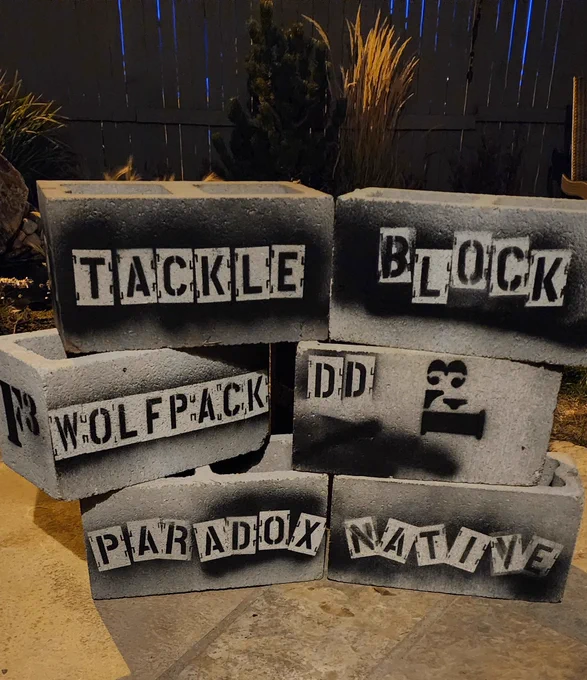 6 cinder blocks lined up with a name spray painted on each in black stencil.