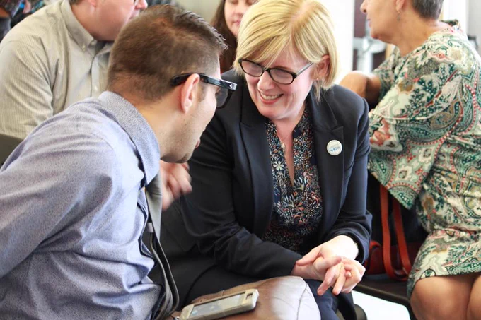Minister Qualtrough sits indoors with a man. They are facing each other and smiling.