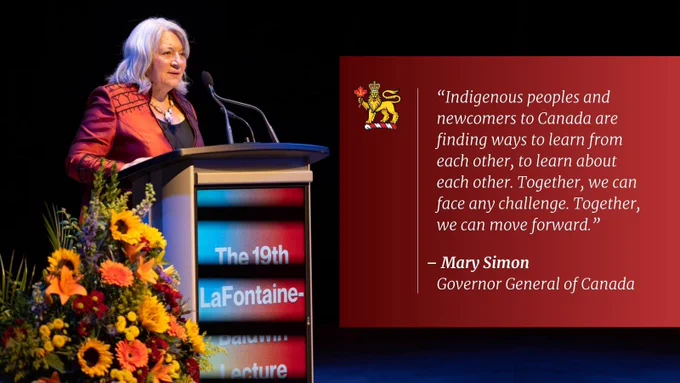 Governor General Mary Simon is on a stage. She is speaking into a microphone. There is a large pot of flowers next to her. There is a red box on the right side of the image. Text in the box reads, “‘Indigenous peoples and newcomers to Canada are finding ways to learn from each other, to learn about each other. Together, we can face any challenge. Together, we can move forward.’ – Mary Simon, Governor General of Canada.” There is a viceregal lion in the upper left corner of the box.