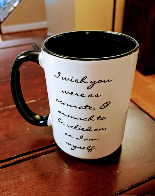 White coffee mug with black handle that says in handwritten, cursive font: "I wish you were as accurate and as much to be relied on as I am myself"