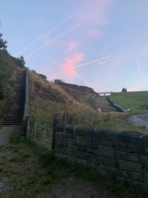 Set of stone steps on the left and on the right the reservoir slipway. The sky has criss crossing plane trails and clouds in bright pink as the sun starts to set.