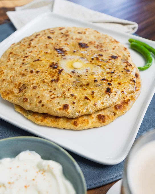 Aloo Paratha with butter on top, and a small bowl of yogurt.