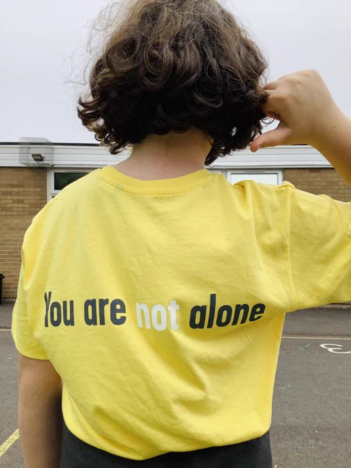Young person wearing a t-shirt that says 'you are not alone' on the back