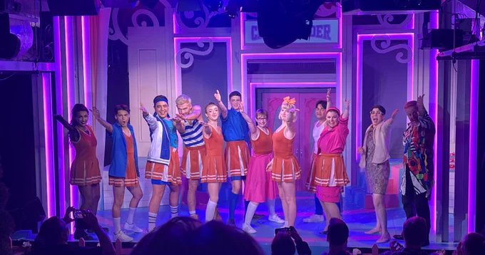 The cast of But I’m A Cheerleader The Musical with their arms pointing towards the back of the auditorium