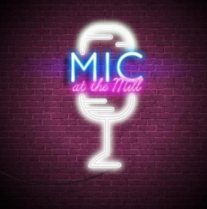 Photograph of a neon sign in the shape of a vintage microphone in white, with the words Mic at the Mill in blue and pink lights. 