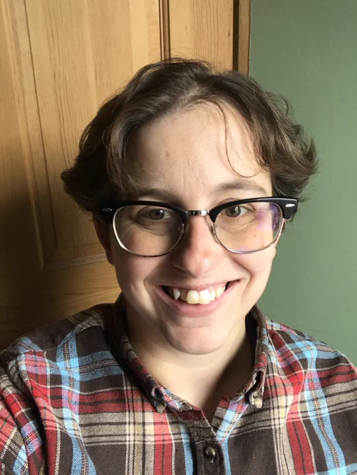 A photo of me, a white person with short light brow hair, glasses, and a red and brown flannel shirt.