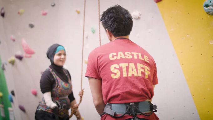 A woman talking to her climbing instructor ready to climb up an indoor wall 
