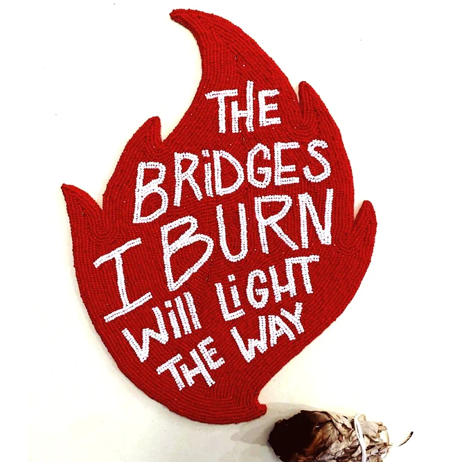 Beaded lettering, white text on red flame. Reading "the bridges i burn will light the way"