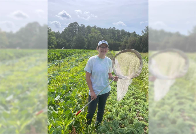 Madison Milotte stands in a field on the farm where they collected cabbage white butterflies and holds a butterfly net.