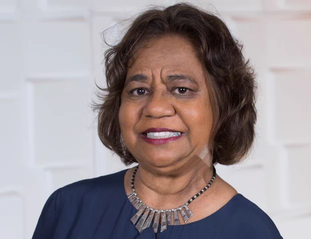 An Aboriginal Australian woman with bobbed black hair smiles at the camera. She is wearing a navy top and silver and black necklace.