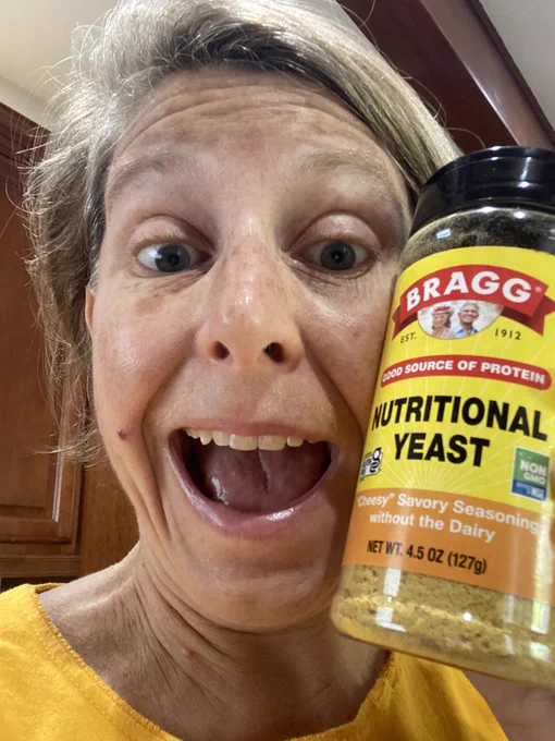 White lady holding up a container of Bragg’s nutritional yeast with a look of shock.