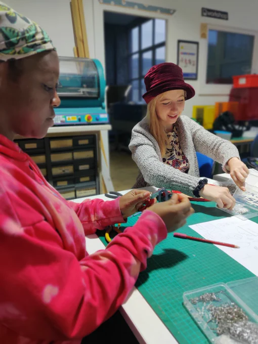 Two people sitting around a workshop table, assembling jewellery and keyrings from recycled plastic 