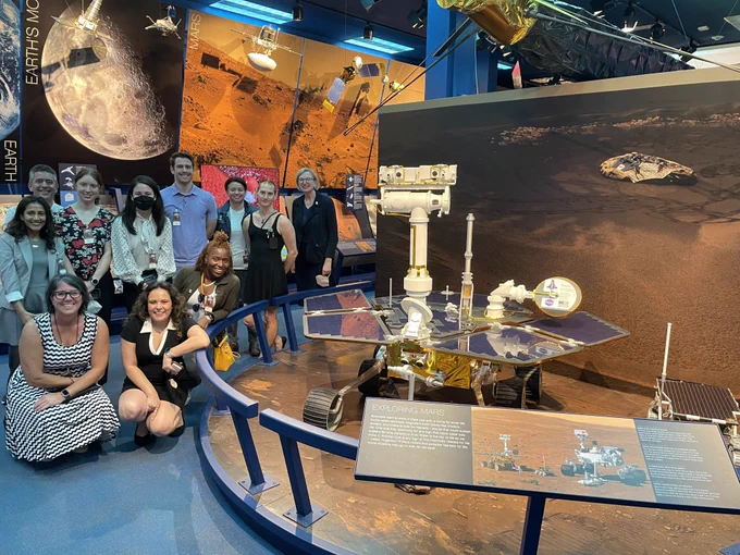 Various TOPS team members and panelists posing for a photo with the Mars Rover in the JPL Visitor Center. 