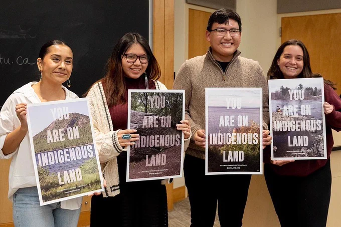 Four students hold up "You Are On Indigenous Land" posters for Indigenous People's Day.