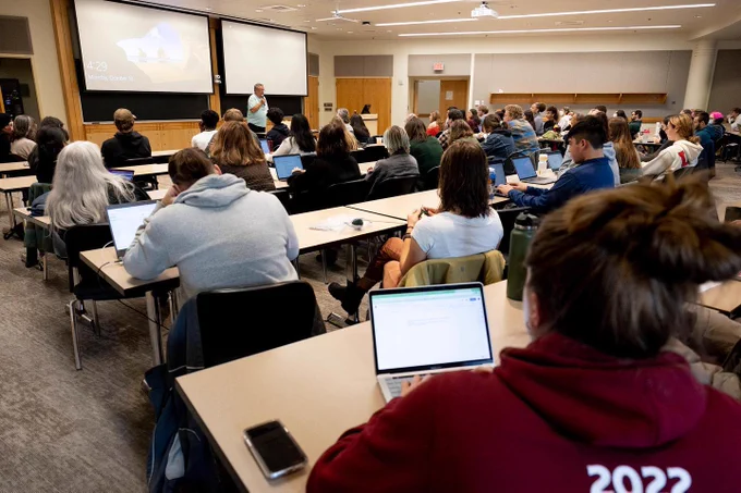 A room full of students watch and listen during an Indigenous People's Day lecture.