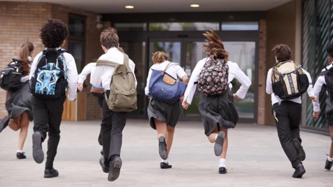 Image depicts a group of children running towards a school.