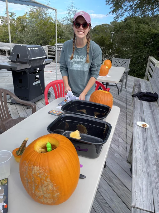One student smiles while carving a pumpkin