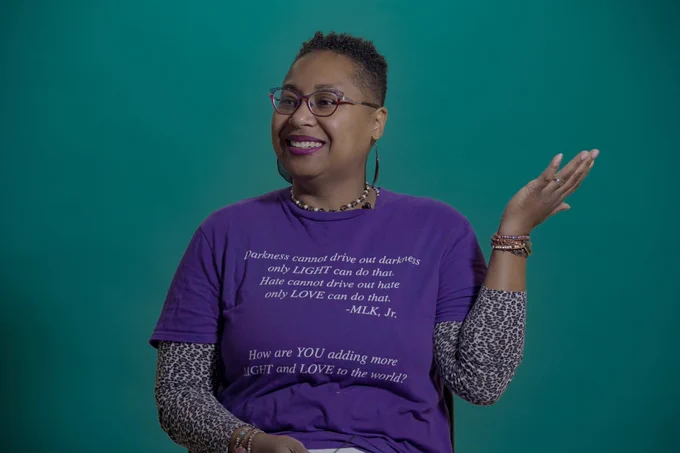 Kevonya Elzia talking during her interview about her work. She's wearing a purple shirt with a green backdrop