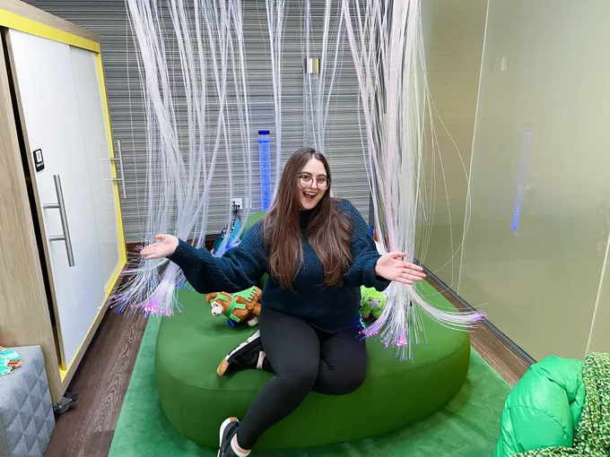 Morgan posing in the tech lab, sitting in the sensors y zone with lush green furniture, pretty lights, and fidget toys.