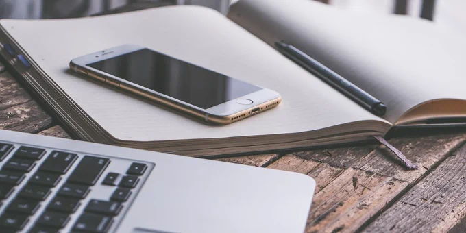A mobile phone sits on an open notebook next to a laptop