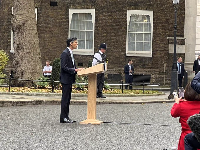 Rishi Sunak at podium with Larry the Cat in the distance