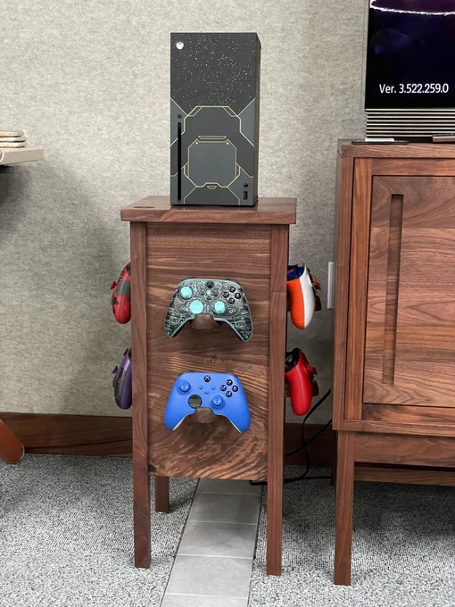 A custom wooden stand that is about 2 feet high with an Xbox series X at the top and six game controllers hanging from the sides