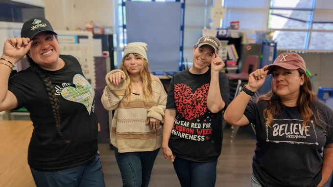 4 teachers standing in a row. 3 wearing hats and grabbing the brims, and 1 wearing a cat beanie while posing like a cat!