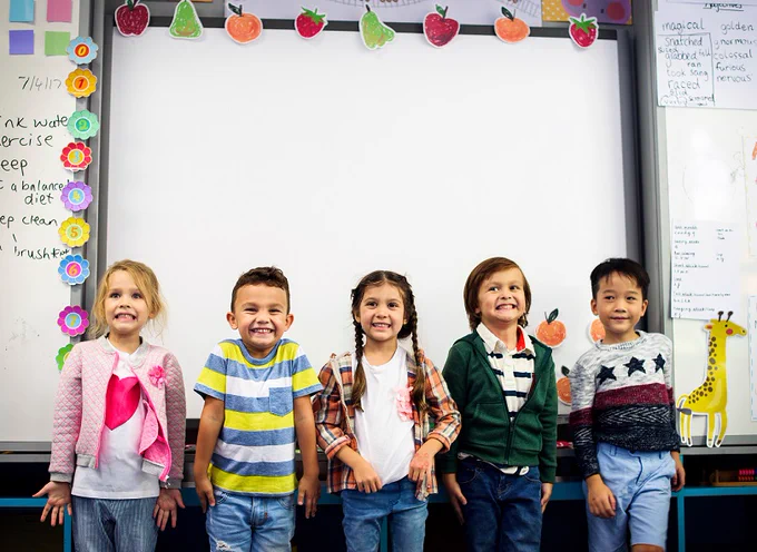 Five children standing in front of a whiteboard. They are smiling for the camera.