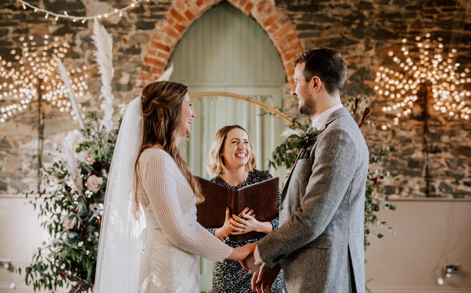 A wedding ceremony where the celebrant is grinning at the bride and groom