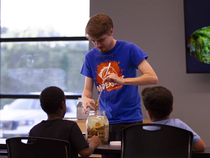 Dalton Lawing, president of UTA’s Herpetology Club, uses tongs to remove a preserved horned lizard from a jar while a pair of young learners watch.