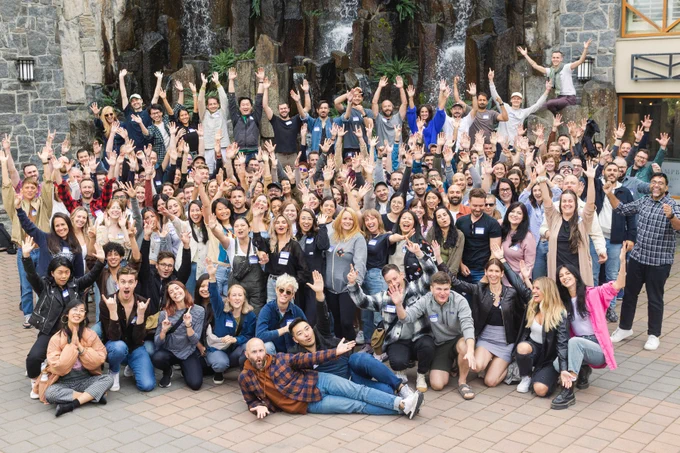 150  MetaLabbers posing in front of a fountain in Whistler BC for Summit 2022. Everyone has big smiles and you can feel their excitement to be back together after three long years apart.
