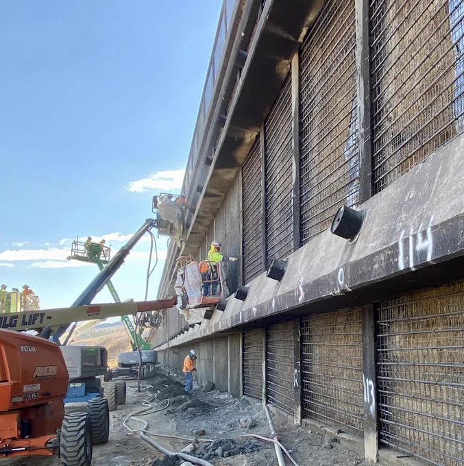 A picture of crews working on lifts to repair a retaining wall.