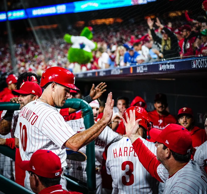 J.T. Realmuto high-fiving his teammates in the dugout after scoring a run. He's wearing the red pinstripes uniform.