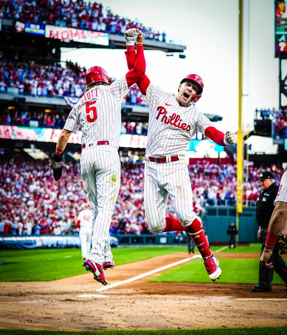 Rhys Hoskins and Bryson Stott jumping in celebration after Hoskins hit a three-run home run. Rhys is yelling. They're wearing the red pinstripes uniform.