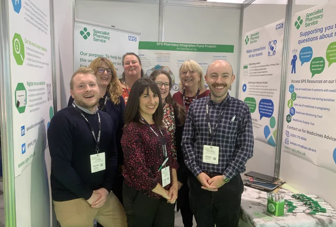 Seven people standing in front of posters about NHS Specialist Pharmacy Service. They are smiling at the camera.