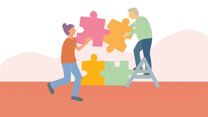 Two people working together to build four giant jigsaw pieces. 