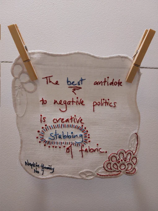 Vintage white cotton doily with new stitching spelling out "The best antidote to negative politics is creative stabbing of fabric"