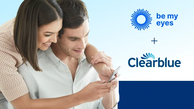 A couple hugging and reading information on a phone, with the Be My Eyes and Clearblue logo on their right.