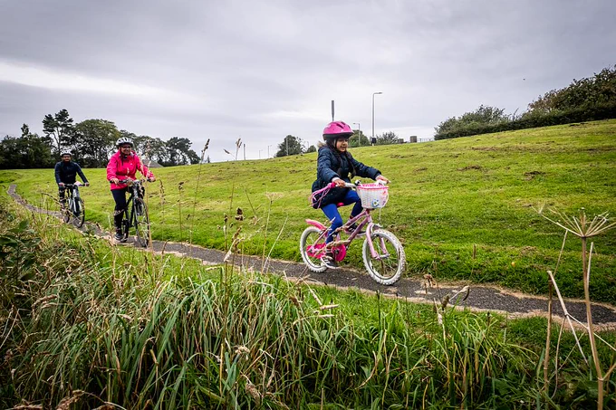 A girl cycling with her parents through a park
