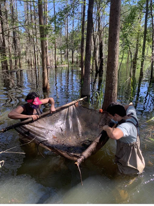 Two individuals holding up a swine after fishing in a Natural Teaching Area. Individual ok the left is wearing a pink visor, waders and black tshirt on the right a blue t-shirt and waders.